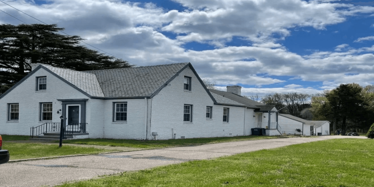 White house with a sloped roof, large lawn, and cloudy blue sky background