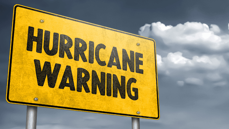 A yellow warning sign displaying "HURRICANE WARNING" against a cloudy gray sky