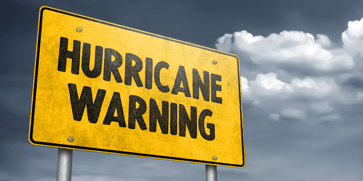 A yellow warning sign displaying "HURRICANE WARNING" against a cloudy gray sky
