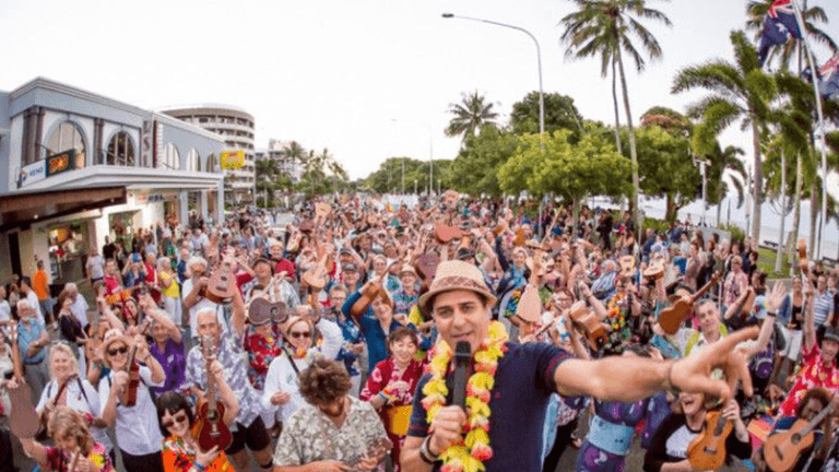 Large crowd of people playing ukuleles outdoors during a festive gathering in a city