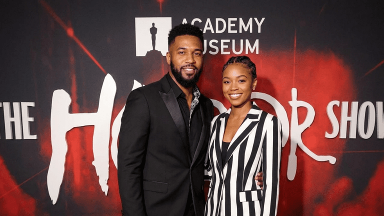 A man and woman pose together on a red carpet at an event.