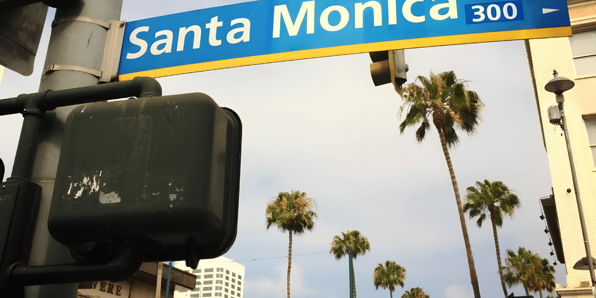 Santa Monica street sign with palm trees and a cloudy sky in the background
