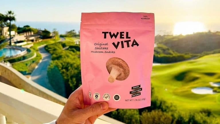 A person holds a pink mushroom snack pouch overlooking a scenic golf course and ocean.