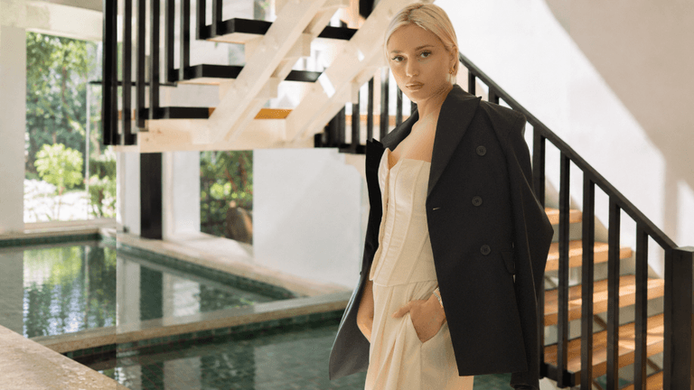 A woman in a stylish outfit poses near a modern staircase and pool.