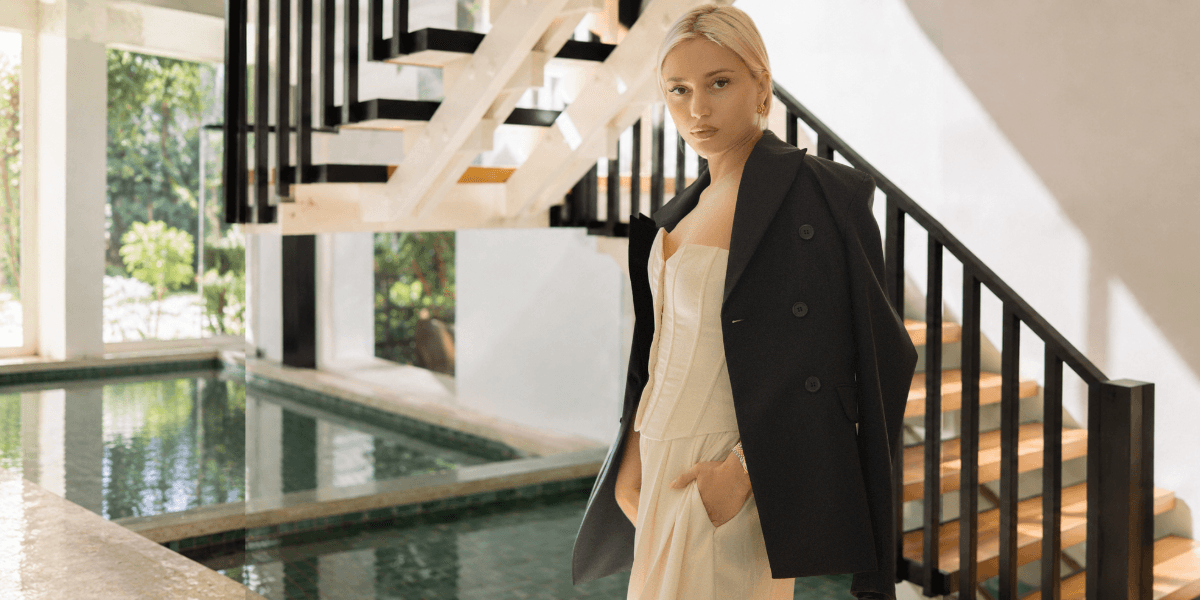A woman in a stylish outfit poses near a modern staircase and pool.
