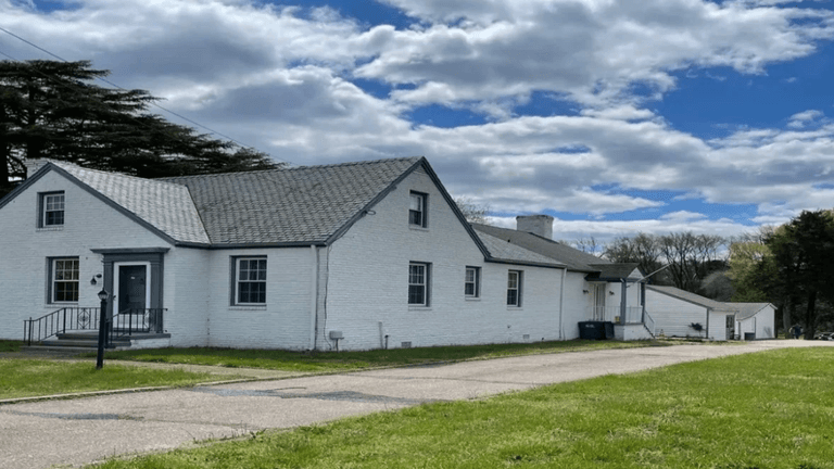 White house with a sloped roof, large lawn, and cloudy blue sky background