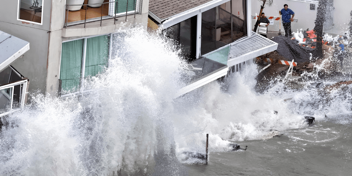 Waves crash against a building, causing damage and flooding near the water's edge
