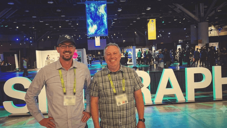 Two attendees standing in front of the illuminated SIGGRAPH sign at the SIGGRAPH 2026 conference in Los Angeles.